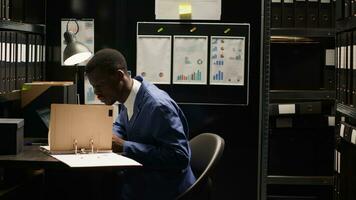 Focused african american agent using laptop for conducting investigation in office. Black policeman utilizes technology for analyzing evidence, reviewing files, photos, and profiling suspect. photo