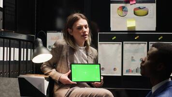 Caucasian private detective holds tablet with greenscreen, as black policeman examines an isolated copyspace display. In office, two detectives utilising digital device with chromakey mockup template. photo