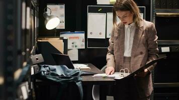 Detective inspector analyzing evidence in an office space filled with files and folders. Private investigator reviews statements on laptop, carrying out meticulous detective work with professionalism. photo