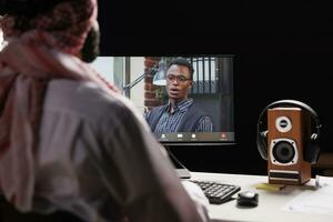 Selective focus on the computer screen showcasing a video call between the Muslim businessman and his AfricanAmerican coworker. The image shows young men utilizing modern technology. photo