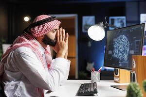 Arab man at desk uses advanced technology to develop secure software, utilizing AI, machine learning, and cloud computing. He ensures cyber security and works with code and programming. photo