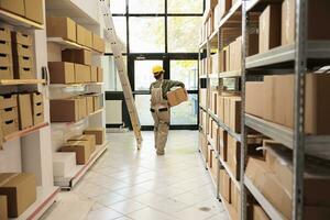 Stockroom worker carrying carton boxes during inventory, wearing protective overall while working in warehouse. Storage room manager checking customers orders before preparing delivery photo