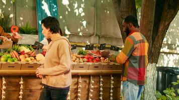 Old male vendor working with young seller at farmers market stall, arranging boxes of produce and price tags on stand. Senior farmer selling organic eco products, homegrown food. photo