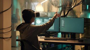 Asian hacker creating malware with vr glasses at night, using virtual reality to hack government server. Young criminal doing cyber espionage on dark web network, illegal phishing. photo