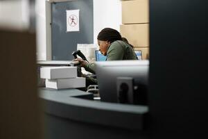 African american supervisor checking metallic box before shipping products to customer, analyzing order quality control in warehouse. Storage room employee wearing industrial overall during inventory photo