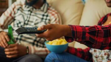 Girlfriend switching channels on television to find movie, using tv remote control to watch favorite film or show with man. Young couple eating chips and drinking beer at home. Close up. photo