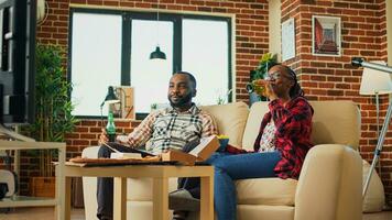 Life partners watching movie on tv together, drinking alcohol and eating snacks at home. Young couple feeling relaxed with film on television and multiple types of fast food from delivery. photo