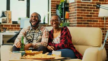 Smiling people laughing at comedy film on television, feeling happt spending time together. Young life partners enjoying movie on tv, eating chips and takeaway food. Tripod shot. photo