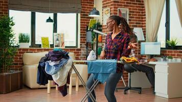 Young girlfriend enjoying doing ironing work at home, having fun listening to music and ironing laundered clothes. Cheerful woman dancing and singing while she does chores, cleaning. photo