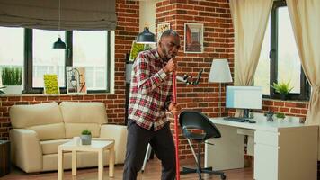 Happy male person dancing and washing floors with washing solution, using mop to sweep dust and dirt in apartment. Young man using cleaning tools to do housework and chores, singing. photo