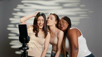 Group of interracial women having fun with photos, embracing imperfections and promoting self acceptance. Funny confident girl taking pictures on smartphone, body diversity in studio. photo