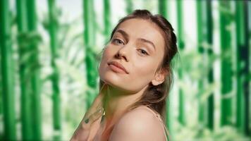 Young gentle woman posing over bamboo trees backdrop, promoting beauty cosmetics for skincare ad campaign. Positive confident lady advertising luminous and radiant look, bodycare products. photo