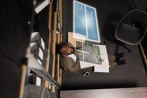 African american man examining augmented reality clues, checking evidence and case files in private investigation space. Male detective trying to solve crime with artificial intelligence hologram. photo