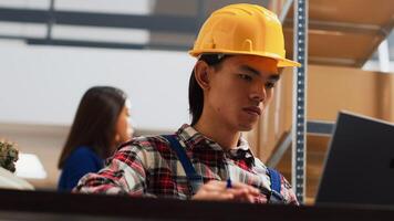 Team of asian people working in storage room with goods, preparing products in boxes for retail store distribution. Employees checking stock of merchandise in warehouse space. Handheld shot. photo