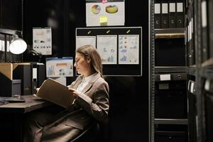 Businesswoman reading corporate files, working late at night at office bookkeeping in storage room. Caucasian manager discovering new bureaucracy report, organizing accountancy documents photo