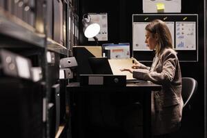 Manager organizing corporate depository, analyzing accountancy report checking administrative record. Businesswoman reading bookkeeping documents, working late at night in storage room photo