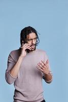 Confused arab man talking on mobile phone and hearing bad news. Puzzled person having communication on smartphone and listening to collocutor with unsure facial expression photo