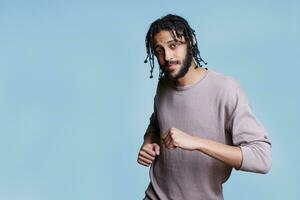 Carefree arab man dancing, making moves with hands and looking at camera. Young handsome arabian person wearing casual clothes in good mood enjoying party and relaxing portrait photo