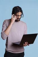 Puzzled arab programmer solving code problem on laptop and rubbing head. Young adult person with unsure facial expression holding portable computer and developing software photo