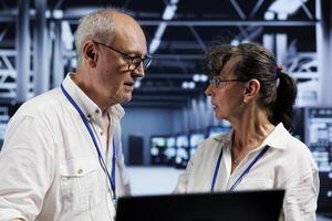 Elderly coworkers preventing strain on data center machines caused by AI applications driving up power usage. Teamworking colleagues maintenancing server clusters doing intense computations photo