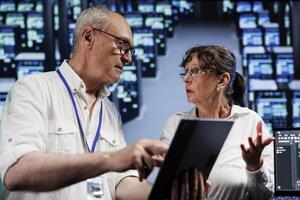 Elderly servicemen running analysis on supercomputers helping businesses manage databases, host websites and store files. Meticulous repairmen auditing high tech server farm electronics photo