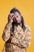 Puzzled man brainstorming job ideas, thinking at solution to solve difficult business problem. Thoughtful african american adult having unsure expression, standing in studio over yellow background photo