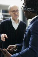 African american worker checking stylish shirt inventory on tablet computer for senior client in shopping centre. Elderly man buying formal clothes and fashionable merchandise in modern boutique photo