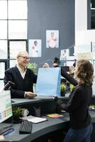 Senior shopper buying fashionable clothes in mall store, making electronic payment at counter desk. Cheerful client talking to store worker discussing casual wear promotions, commercial activity. photo