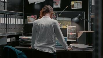 Private investigator examining criminal clues files on map in archive room, reading suspicious information. Law enforcement agent studying forensic evidence to catch crime suspect. photo