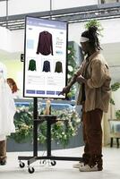 Shopper looks for clothes on monitor kiosk service in fashion boutique at mall. Male customer shopping for clothing line items in retail store, touch screen board for self service concept. photo