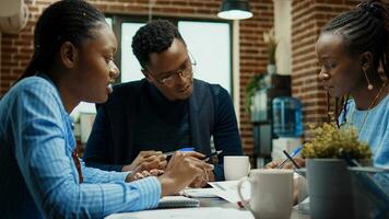 Company employees reviewing documents in briefing meeting office, examining papers with corporate information. African american people working on new company vision in coworking space. photo