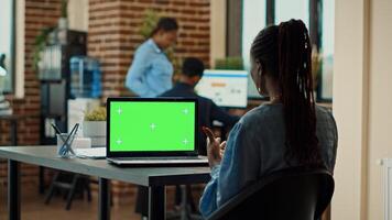 Corporate person using green screen in office, checking business information on isolated display. Young woman working with chroma key coyspace on laptop, blank mockup template. photo