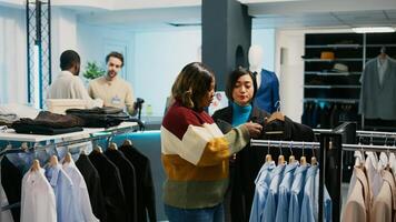 Asian retail worker helping client to choose clothes, using tablet to check merchandise stock in department store. Shop assistant showing new formal wear collection to female customer. photo