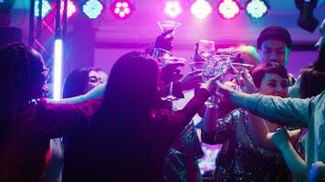 Happy diverse people clinking glasses at disco party, drinking alcohol and saying cheers on dance floor. Men and women partying and having fun at nightclub, raising drinks at event. photo