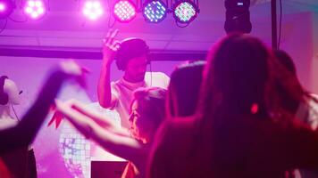 Male DJ partying with people at club, mixing music on audio station to create funky party atmosphere in discotheque. Young man dancing and jumping with friends, having fun on dance floor. photo