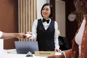 Hotel staff giving access room key card to guests after doing check in process, helping with accommodation in lobby. Two people preparing to see room after registering at reception. photo