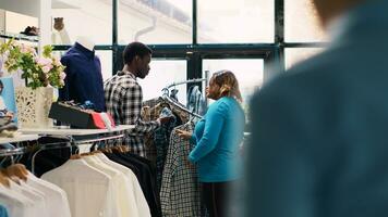 African american couple looking at stylish merchandise, checking clothes fabric in clothing store. Smiling customers enjoying shopping session, buying trendy outfits and accessories in modern boutique photo