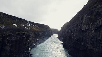 zumbido Disparo de islandés Gullfoss cascada, majestuoso agua corriente fluido Entre rocoso colinas y acantilados hermosa cascada en Islandia corriendo abajo apagado montañas, invierno paisaje. lento movimiento. foto