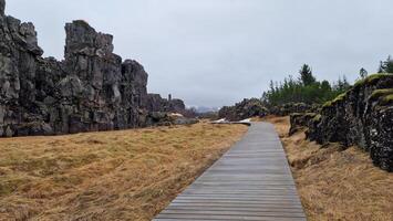 Rocky mountain range in arctic scenery, thingvellir national park with spectacular landscapes and massive cliffs in iceland. Rock formations creating hills in icelandic valley with walkway. photo