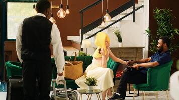 Hotel bellboy offering to carry baggage and help guests with check in process, tourists waiting in lounge area. Professional resort bellhop providing luxury service to travellers. photo