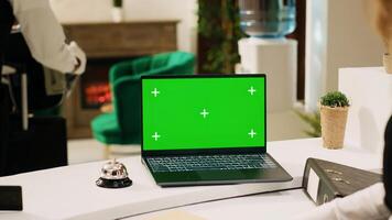 Hotel staff using greenscreen on laptop, working at front desk reception to help people. Receptionist looking at isolated display with blank mockup template, tropical seaside resort. photo