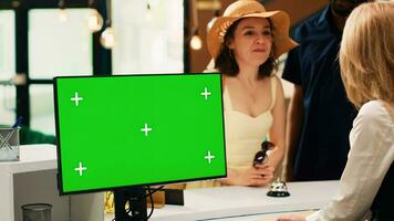 Employee working with greenscreen at hotel front desk, talking to guests at reception. Receptionist using isolated copyspace display with chroma key template, doing check in process. photo