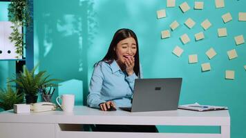 Happy cheerful employee burst out laughing watching laptop screen at work. Lively chipper office clerk having a laugh enjoying herself in colourful relaxed workplace over blue studio background photo