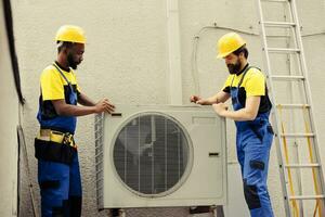 Teamworking certified technicians starting work on broken hvac system, taking apart condenser coil panel. Expert wiremen disassembling air conditioner to check for bad wiring photo