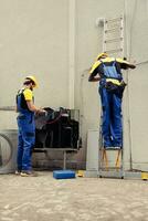 Licensed electrician coworkers doing yearly hvac system investigation, assembling manifold gauges. Precise servicemen looking for freon leaks leading to weaker cooling efficiency photo