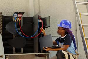 Professional african american worker asked by customer to detect cause of malfunctioning hvac system, keeping track on laptop of nitrogen pressure loss over time using manifold indicators photo