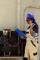 Engineer apprentice offering informations about hvac system parts needing to be replaced to master technician during phone call. Worker checking maintenance plan after repairing broken capacitor photo