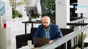 Office manager compares data on laptop to create new report, working with statistics to solve tasks. Unicorn business employee analyzing documents in open space urban building. photo
