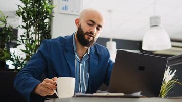 Middle eastern man reads documents online before creating professional marketing report in office. Male worker trying to find business solution, entrepreneur in coworking space. photo