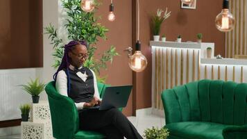 Front desk staff working on laptop in lobby, creating list of guests with room reservations to ensure easy check in process and pleasant stay. African american employee at luxurious hotel. photo